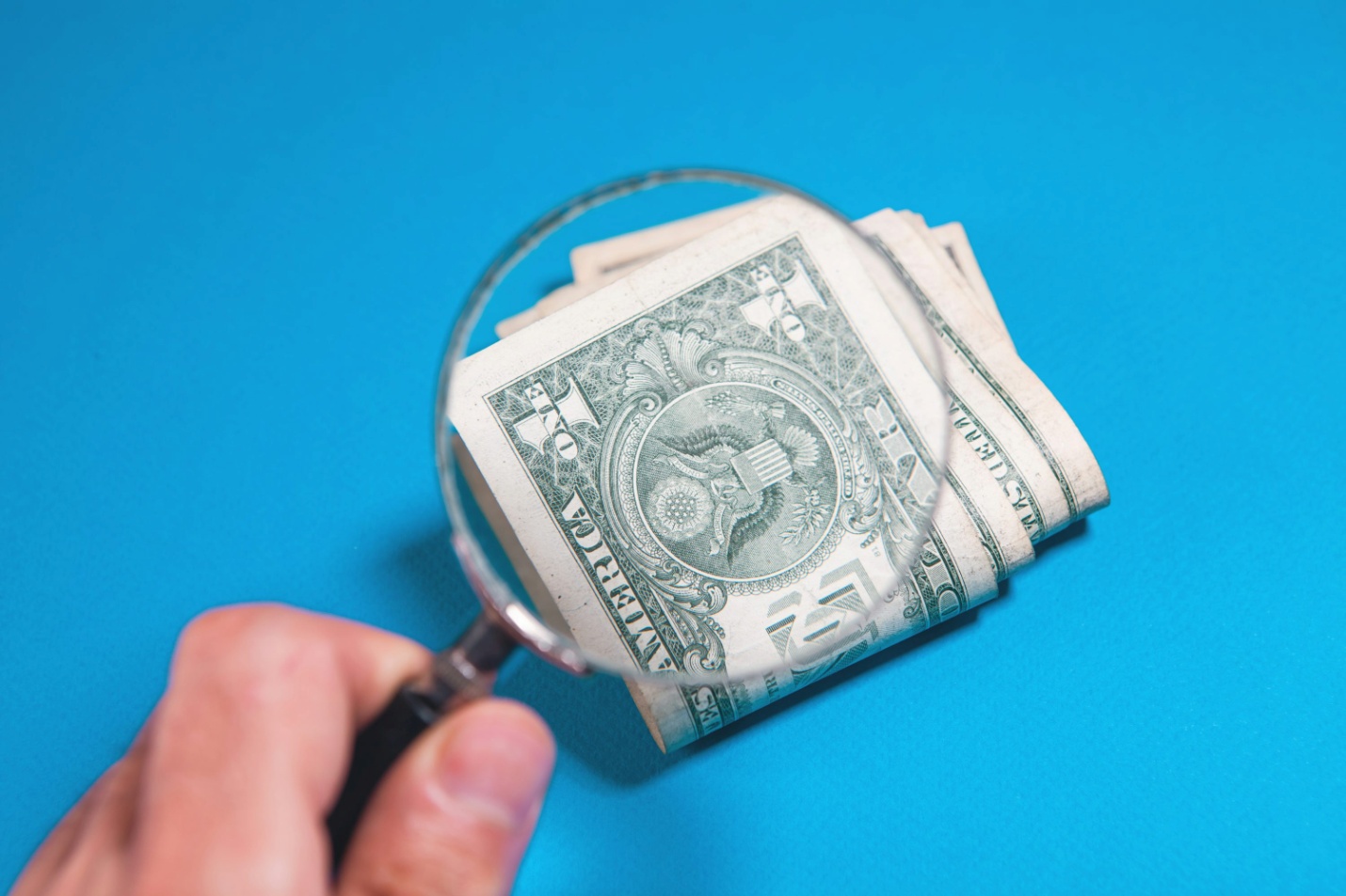 A magnifying glass held over a stack of dollar bills